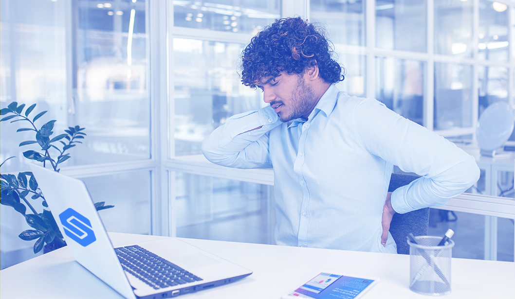 Trabajador de oficina con dolor de espalda mientras está sentado frente a una computadora.