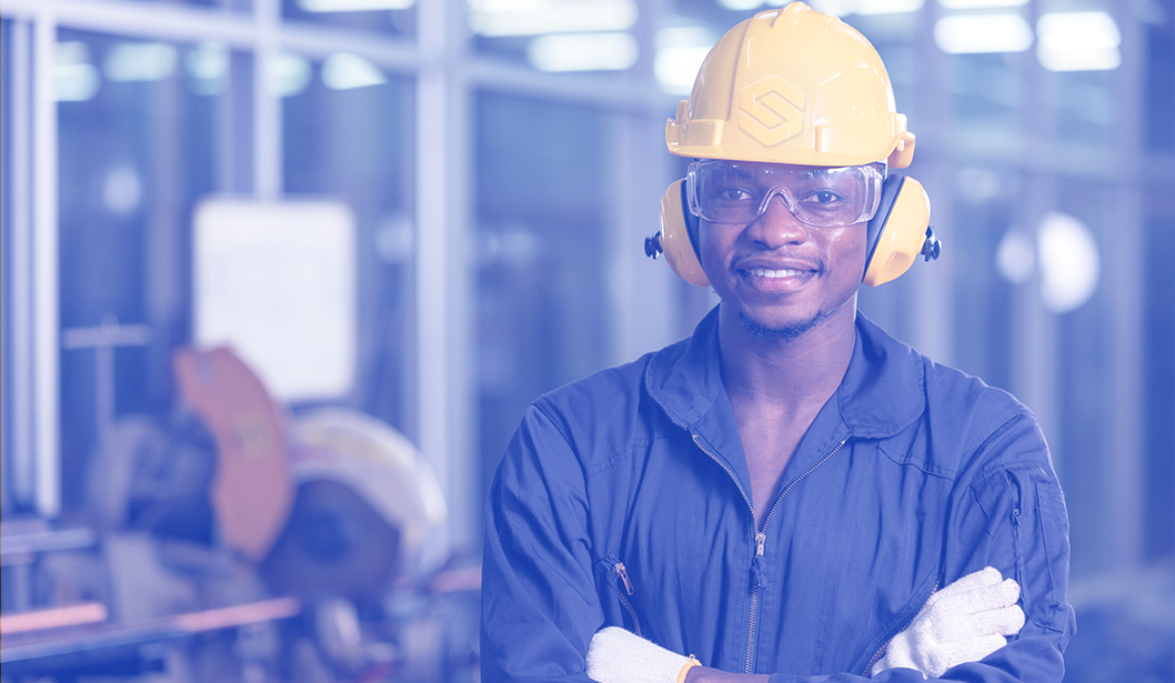 Trabajador industrial con equipo de protección personal, incluyendo casco, guantes y protectores auditivos.